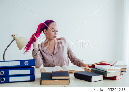 girl with pink hair sitting at a table reading a book 65201233