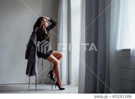 girl with gray coat sits on a Chair looking out of the window 65201306