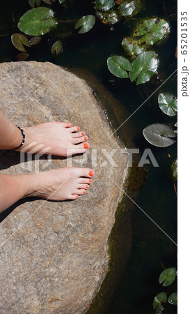 Woman feet on stone near pond - Summer vacation concept 65201535