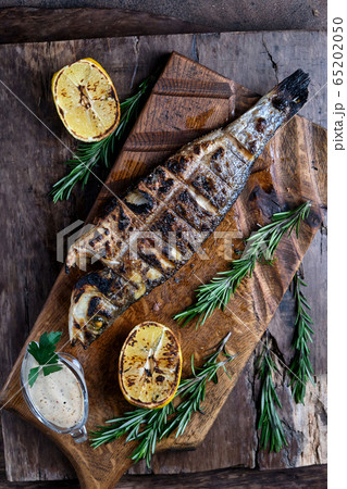 Grilled trout served on a cutting board. On wooden background. Top view 65202050