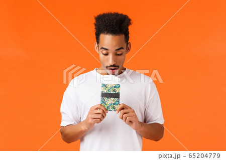 Dreamy and wondered, african-american guy imaging best vacation ever, holding passport with tickets, looking documets amused, standing orange background prepare for flight luxury resort Dreamy and wondered, african-american guy imaging best vacation ever, holding passport with tickets, looking documets amused, standing orange background prepare for flight luxury resort 65204779