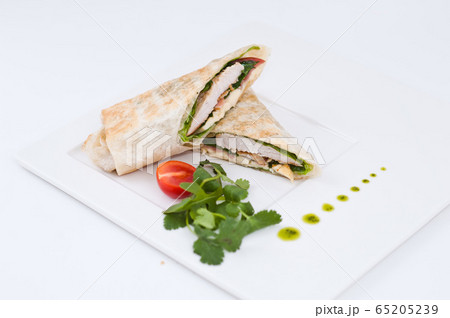 Shawarma chicken roll in a pita with fresh vegetables and cream sauce on white background. Selective focus Shawarma chicken roll in a pita with fresh vegetables and cream sauce on white background. Selective focus 65205239