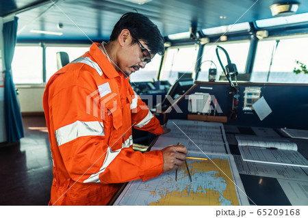 Filipino deck Officer on bridge of vessel or ship. He is plotting position on chart 65209168