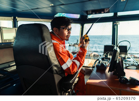 Filipino deck Officer on bridge of vessel or ship. He is speaking on GMDSS VHF radio Filipino deck Officer on bridge of vessel or ship. He is speaking on GMDSS VHF radio 65209370