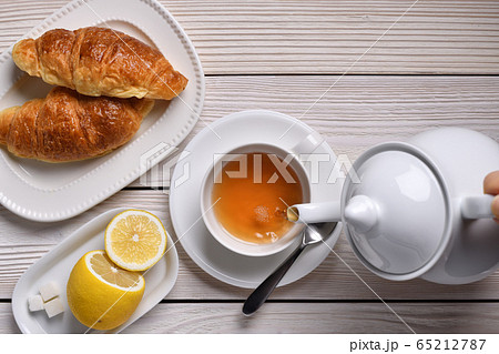 Top view of pouring tea on a cup with lemon and croissants on white table 65212787