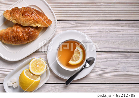 Top view of a cup of tea with lemon and croissants on white table 65212788