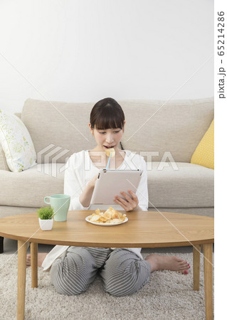 タブレットを見ながらポテチトングでポテトチップスを食べる若い女性 65214286