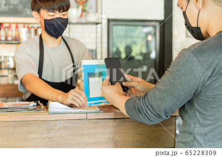 Male customer with protective mask paying bill by cell phone in cafe. Male customer with protective mask paying bill by cell phone in cafe. 65228309