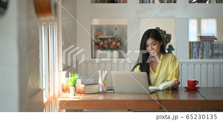 Photo of woman sitting and taking note while sitting in front her computer laptop. 65230135
