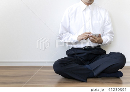床に座ってスマートフォンを操作しているワイシャツを着た男性 65230395