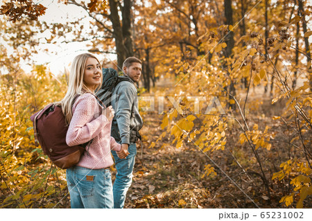 Smiling couple of tourists walking along a forest path holding hands and looking back at camera Smiling couple of tourists walking along a forest path holding hands and looking back at camera 65231002