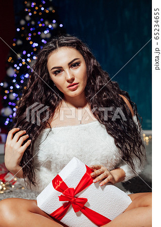 Beautiful fashionable brunette woman at the Christmas tree with gifts for the new year Beautiful fashionable brunette woman at the Christmas tree with gifts for the new year 65234655