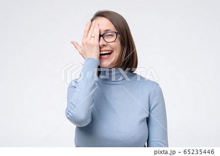 Laughing caucasian woman in glasses covered her face half hand Laughing caucasian woman in glasses covered her face half hand 65235446