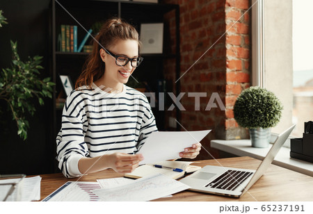 Young cheerful woman revising papers while working 65237191