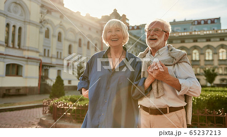 Happy and beautiful senior couple holding hands and smiling while standing outdoors together Happy and beautiful senior couple holding hands and smiling while standing outdoors together 65237213