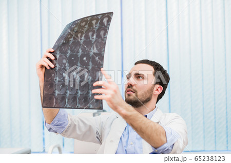 Portrait of a handsome caucasian male radiologist holding x-ray while sitting at his office 65238123