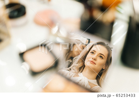 Close-up of face of young woman reflected in mirror of powder on woman table, looking away. 65253433