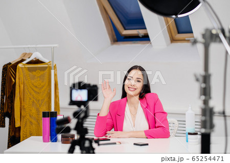 A female beauty blogger records a video in a white room. Lighting and camera on a tripod. 65254471