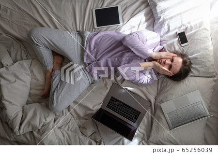 woman trying to work being ill staying at home on bed with computer on the bed. 65256039