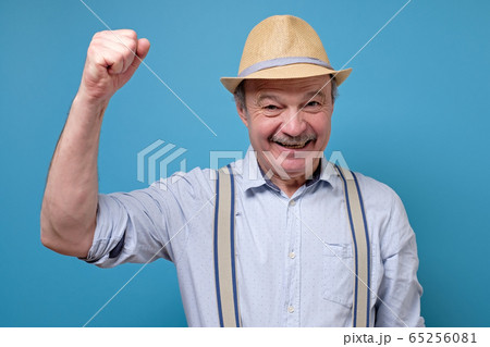 Senior hispanic man in summer hat raising fist up celebrating his success. Senior hispanic man in summer hat raising fist up celebrating his success. 65256081
