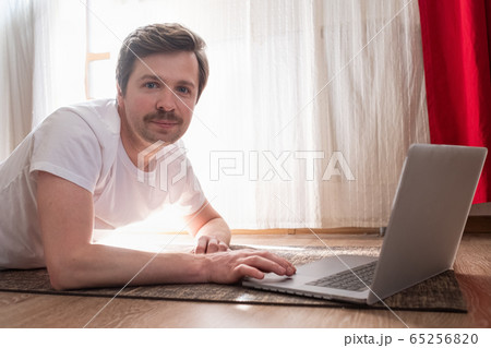 Handsome strong sportsman on floor in living room using laptop computer 65256820