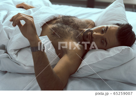 Handsome man checking time after waking up Handsome man checking time after waking up 65259007