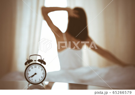 Woman stretching hands in bed after wake up, sun flare . Brunette entering a day happy and relaxed after good night sleep and back view. Concept of a new day and joyful weekend 65266579