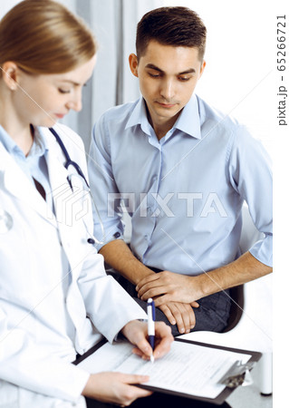 Female doctor holding application form while consulting man patient in hospital office. Medicine and healthcare concept Female doctor holding application form while consulting man patient in hospital office. Medicine and healthcare concept 65266721