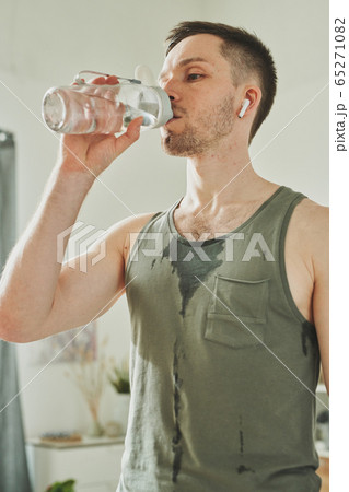 Young sweaty sportsman in earphones and activewear drinking water from bottle Young sweaty sportsman in earphones and activewear drinking water from bottle 65271082
