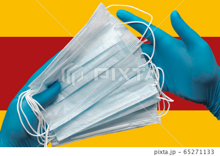 Doctor holds face masks in hands blue gloves on background national flag of Spain. Concept pandemic outbreak, quarantine, hygiene. Surgical antibacterial face bandage 65271133
