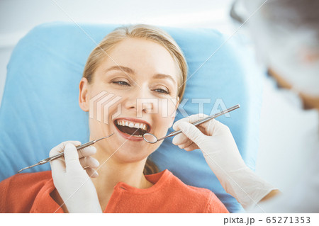 Happy smiling woman is being examined by dentist at dental clinic. Healthy teeth and medicine, stomatology concept Happy smiling woman is being examined by dentist at dental clinic. Healthy teeth and medicine, stomatology concept 65271353