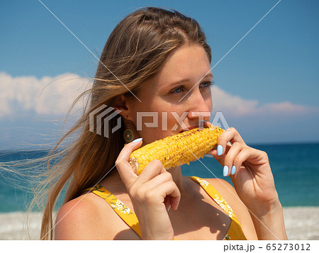 Young woman eating corn on the beach Young woman eating corn on the beach 65273012