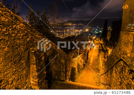Staircase descending into a narrow street with lanterns in evening Genoa, mountains in the background 65273486