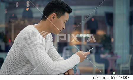 Side view of hamdsome asian man scrolling phone on big mall background 65278803