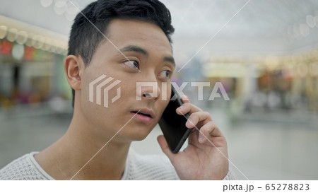 Close up of asian man talking on phone on shopping center background Close up of asian man talking on phone on shopping center background 65278823