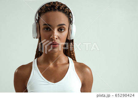 My favourite playlist. Cute and sporty african woman in headphones looking at camera while standing against grey background My favourite playlist. Cute and sporty african woman in headphones looking at camera while standing against grey background 65290424