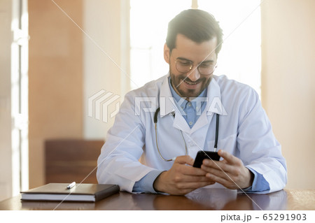 Smiling Caucasian male doctor use smartphone at workplace Smiling Caucasian male doctor use smartphone at workplace 65291903