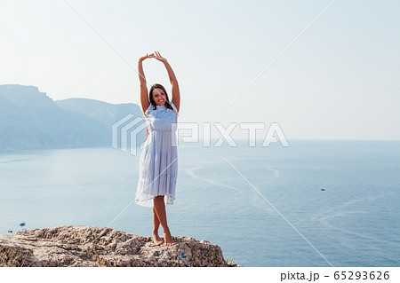 beautiful tanned woman in blue dress on top of a cliff by the sea beautiful tanned woman in blue dress on top of a cliff by the sea 65293626