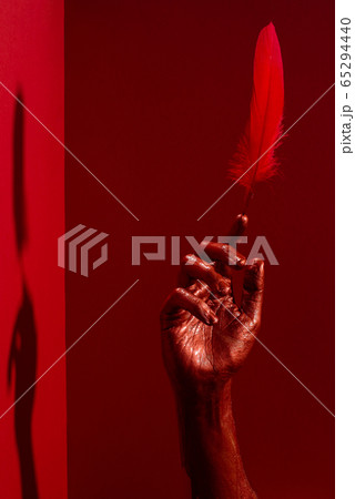 Red hand with feather in finger against vibrant Red hand with feather in finger against vibrant 65294440