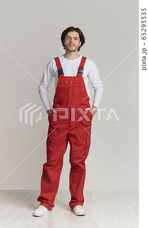 Portrait of young handyman wearing work clothes posing over light background Portrait of young handyman wearing work clothes posing over light background 65295535