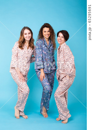 Portrait of three beautiful young girls wearing colorful pyjamas having fun during sleepover isolated over blue background. Pajama party and hen-party concept 65295691