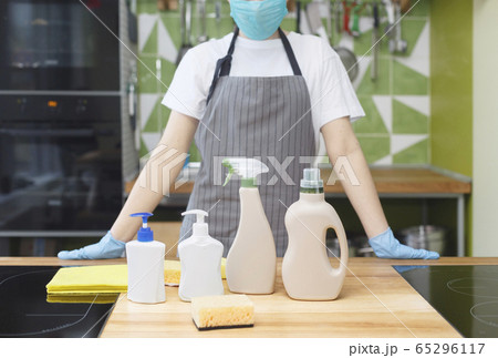 Woman in mask and gloves showing all eco detergents for kitchen disinfection 65296117