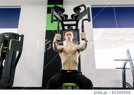 Bodybuilder posing in the gym. Handsome muscular man working out hard at gym. Training without shirt. Chest exercises. Chest workouts. Bodybuilder posing in the gym. Handsome muscular man working out hard at gym. Training without shirt. Chest exercises. Chest workouts. 65300508
