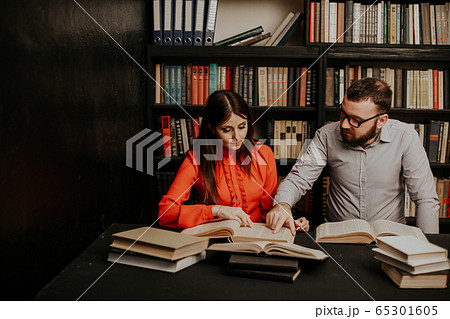 a man and a woman read books in the library are preparing for the exam 65301605