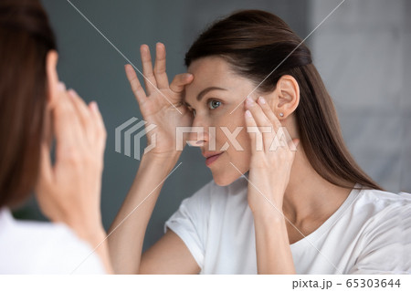 Satisfied woman looking in mirror check face after beauty treatment 65303644