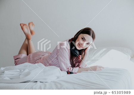 woman in pajamas listening to music with headphones on the bed 65305989