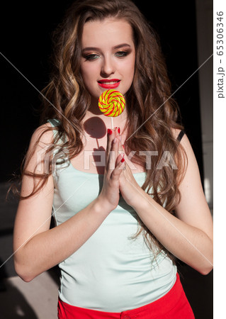 Beautiful fashionable woman eats delicious sweet candy lollipop on a stick Beautiful fashionable woman eats delicious sweet candy lollipop on a stick 65306346