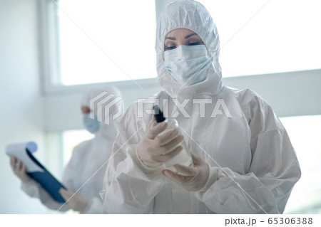 Female medical worker in protective clothing and medical mask holding antiseptic 65306388