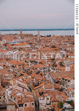 Aerial panoramic view from cathedral bell tower San Marco Campanile of old historical city centre, sea, red tiled roofs and palaces. Venice, Italy - is a popular tourist destination of Europe. Aerial panoramic view from cathedral bell tower San Marco Campanile of old historical city centre, sea, red tiled roofs and palaces. Venice, Italy - is a popular tourist destination of Europe. 65308311