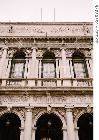 Vintage ornate windows and columns, venetian style, on fragment of building's luxurious building in Venice. Traditional ancient gothic style. Three windows and arches decorated with stucco molding. Vintage ornate windows and columns, venetian style, on fragment of building's luxurious building in Venice. Traditional ancient gothic style. Three windows and arches decorated with stucco molding. 65308376